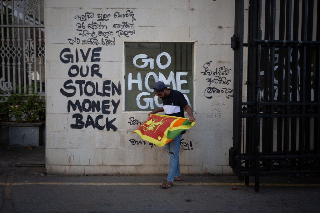 A protester unfurls the Sri Lankan national flag at the vandalized gateway of the presidential palace on July 13, 2022 in Colombo, Sri Lanka. Sri Lanka’s airforce had confirmed then that ex-President Gotabaya Rajapaksa has fled the country on a military jet to the Maldivian capital Male, following days of unrest in which the presidential palace and office were taken over by anti-government protesters. (Abhishek Chinnappa/Getty Images)