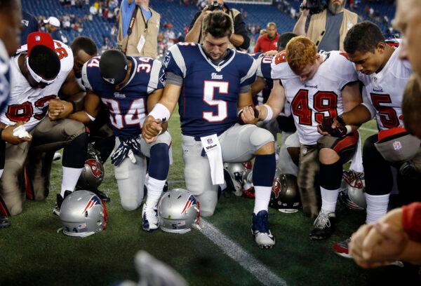 Tampa Bay Buccaneers defensive tackle Gerald McCoy (93), New England Patriots running back Shane Vereen (34), Patriots quarterback Tim Tebow (5), Buccaneers linebacker Joe Holland (49) and Buccaneers quarterback Josh Freeman (5) kneel an pray with others at midfield after an NFL preseason football game in Foxborough, Mass., on Aug. 16, 2013. (Michael Dwyer/AP Photo)