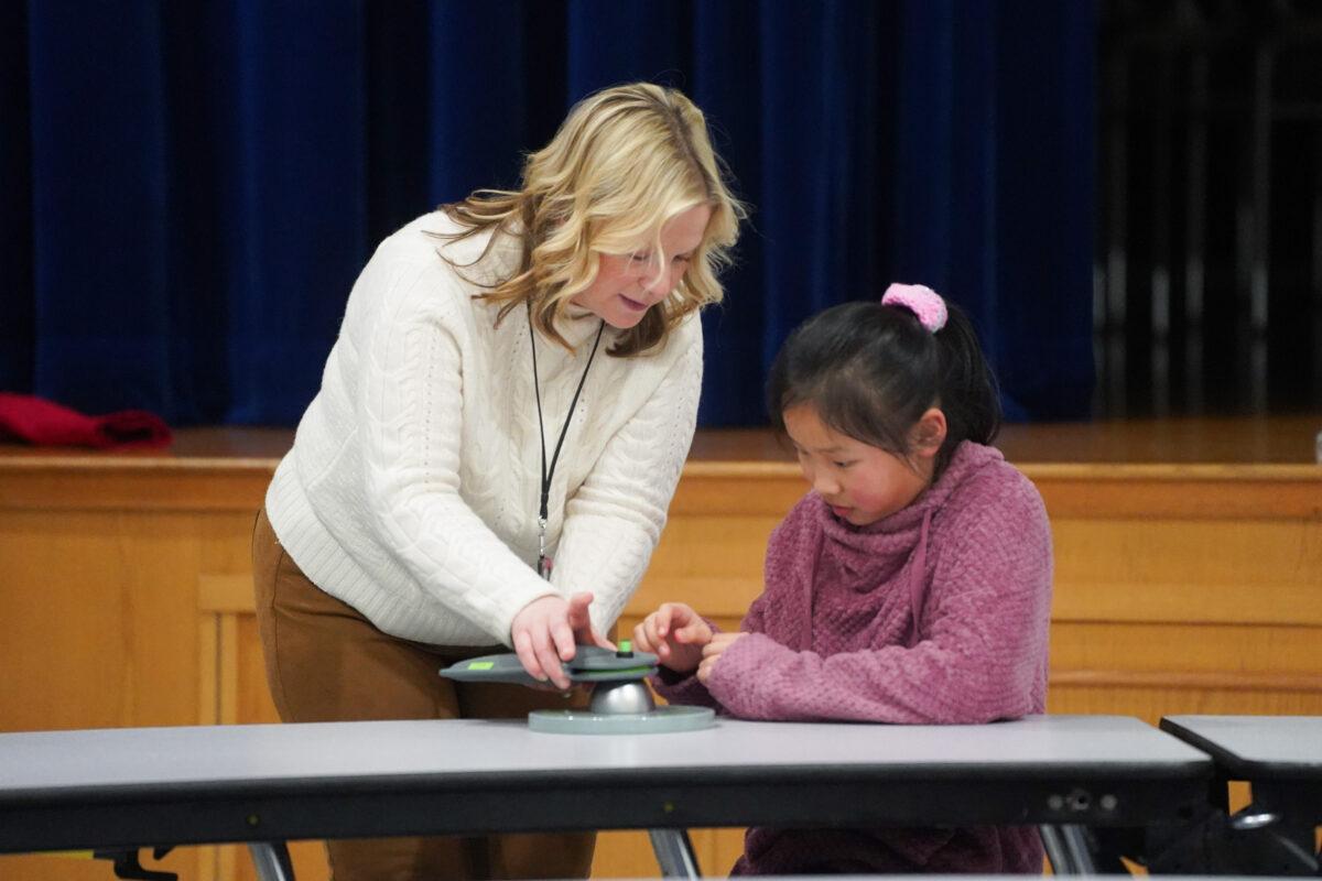 Middletown School District Superintendent Amy Creeden demonstrates how to open a Yondr pouch to a student at Presidential Park Elementary School in Middletown, N.Y., on Feb. 7, 2023. (Cara Ding/The Epoch Times)