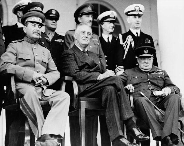 The "Big Three" meet in Tehran, Iran, in December 1943. Front row (L–R): Soviet Union Marshal Joseph Stalin, U.S. President Franklin D. Roosevelt, UK Prime Minister Winston Churchill (wearing his air commodore's uniform) on the portico of the Russian Embassy. Back row (L–R of those visible): Gen. H.H. Arnold, chief of the U.S. Army Air Force; Gen. Alan Brooke, chief of the Imperial General Staff; Adm. Cunningham; Adm. William Leahy, chief of staff to Roosevelt, during the Teheran Conference. Library of Congress. (Public Domain)
