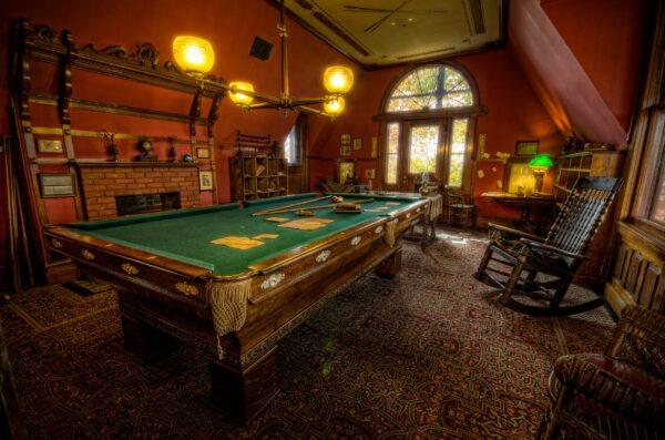 Although it's referred to as the “billiard room,” this was most often used by Clemens as his study. Howard said that “as an avid player, Sam would have protected the playing surface of the table, especially as he frequently used it as a supplemental work surface.” The ceiling of the room is adorned with the top of a billiard table, and light streams into the space. A traditional brass lighting fixture hangs over the billiard table. (Courtesy of the Mark Twain House)
