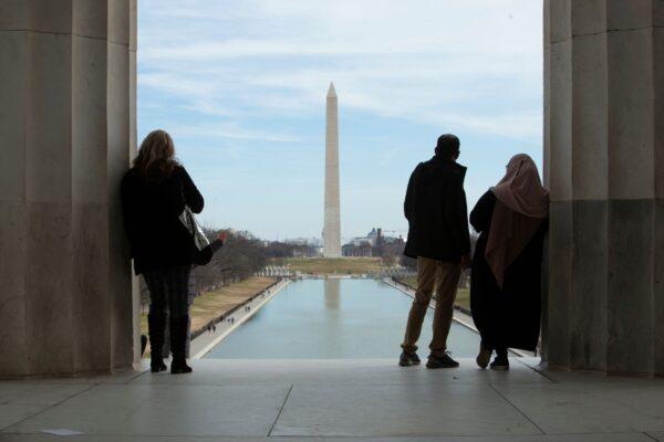 A couple and a mother and son stand at the top of the memorial stairs looking out over the National Mall. (J.H.Smith/Cartiophotos)