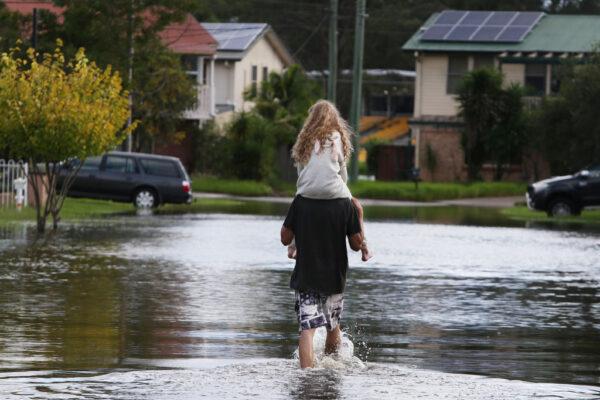 A man and his daughter walk through floodwaters to return to their family home in Windsor, Sydney, Australia, on March 9, 2022. (Lisa Maree Williams/Getty Images)