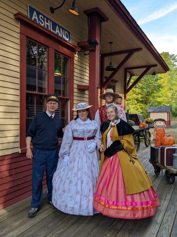 Jim Cluett (L), the conductor for the scenic train, with reenactors (L–R) Winnifred in the white dress, John in the straw hat and crimson vest, and Sue in her stunning red dress and goldenrod wool coat. (Courtesy of Tim Carter)