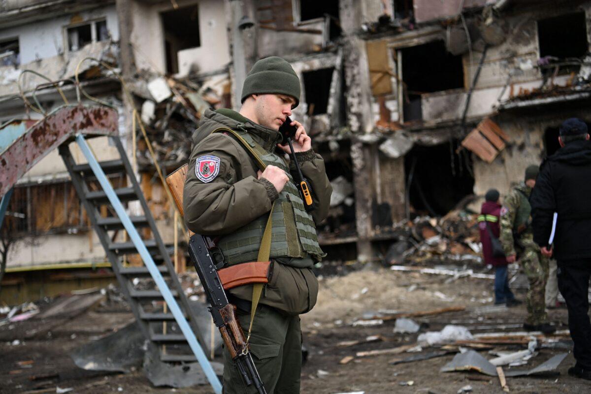 A Ukrainian serviceman talks on a smartphone in front of a damaged residential building at Koshytsa Street, a suburb of the Ukrainian capital Kyiv, where a military shell allegedly hit, on Feb. 25, 2022. (Daniel Leal/AFP via Getty Images)