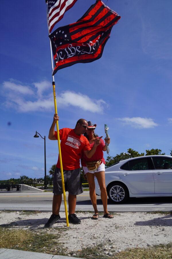 Derek Arnold of Ocala, Fla., conducts live podcasts while waving his flags on Southern Boulevard Bridge near Mar-a-Lago in Palm Beach, Fla., on March 31, 2023. (John Haughey/The Epoch Times)