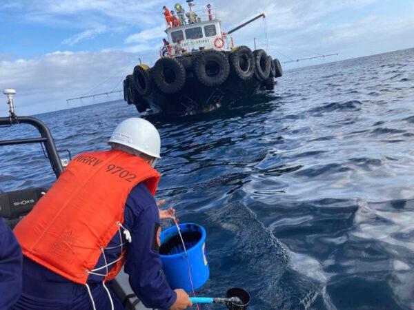 A coast guard personnel collects water samples from an oil spill in the waters off Naujan, Oriental Mindoro, central Philippines, on March 2, 2023. (Philippine Coast Guard via AP)