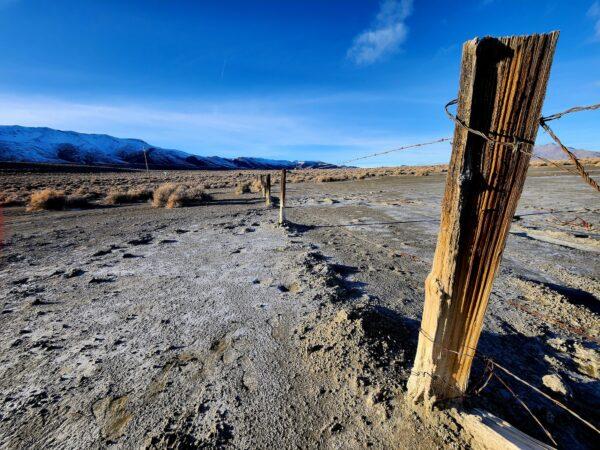 A barren lake bed stretches for miles on the way to Fortitude Ranch Nevada. Below, manager Brandon M. walks along the dirt road to the main ranch house on March 2, 2023. (Allan Stein/The Epoch Times)