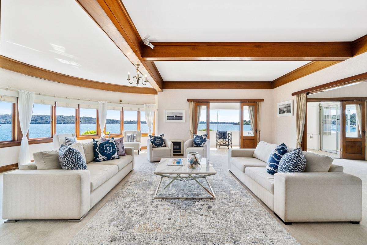 The airy living room features gleaming exposed wood beams, and a wall of huge windows affording a grand view of the surrounding waters. (Courtesy of Sydney Sotheby's International Realty)