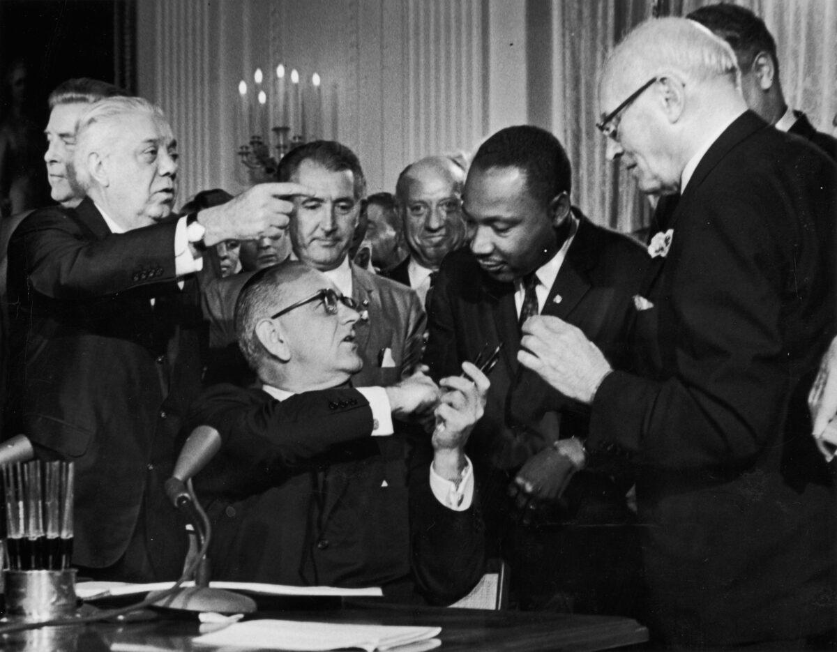 President Lyndon B. Johnson shakes the hand of Dr. Martin Luther King Jr. at the signing of the Civil Rights Act while officials look on in Washington on July 2, 1964. (Hulton Archive/Getty Images)