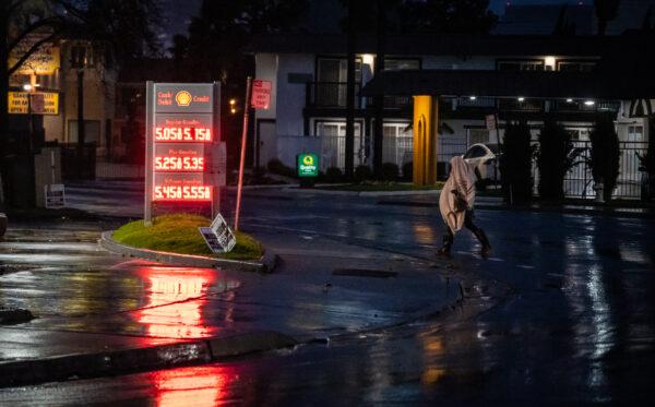 A homeless man walks by a gas station during a rainstorm in Sacramento on March 9, 2023. (John Fredricks/The Epoch Times)