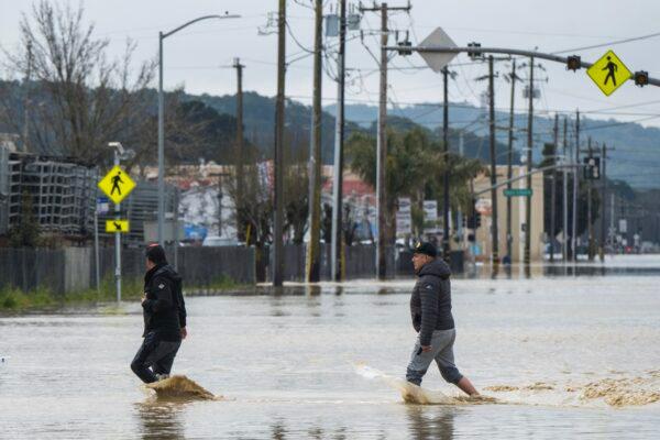People walk through floodwaters in Watsonville, Calif., on March 11, 2023. Gov. Gavin Newsom has declared emergencies in 34 counties in recent weeks, and the Biden administration approved a presidential disaster declaration for some on Friday morning, a move that will bring more federal assistance. (AP Photo/Nic Coury)