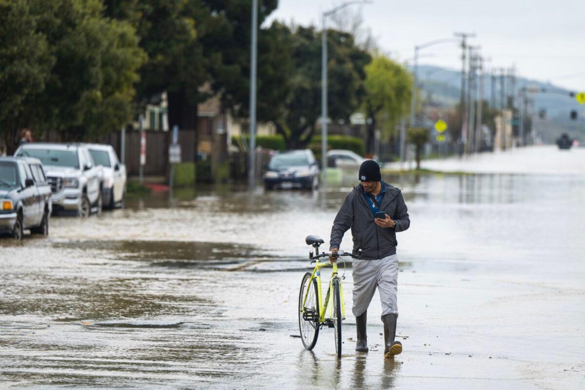 A man walks his bicycle through floodwaters in Watsonville, Calif., on March 11, 2023. (Nic Coury/AP Photo)