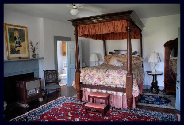 The grand Federal period, heavily carved, four-poster bed sports a ruffled insert. Historically, privacy curtains were sometimes tucked into the ruffle and let down if the person using the bed so desired. This room includes a mirrored armoire and a needlepoint-covered chair. (Courtesy of Michael Johnson)