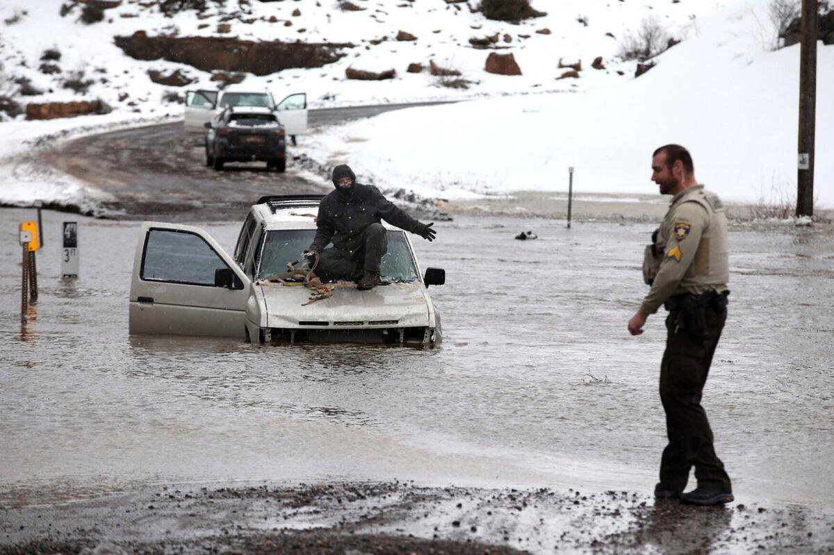 A driver speaks with a law enforcement official from the hood of his car after getting swamped while attempting to cross a wash in Flagstaff, Ariz., on March 22, 2023. (Jake Bacon/Arizona Daily Sun via AP)