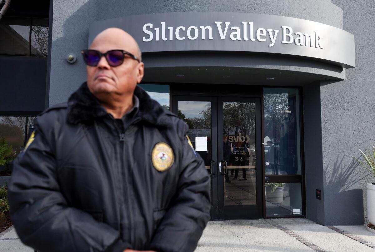 A security guard at the failed Silicon Valley Bank monitors a line of people outside the office in Santa Clara, Calif., on March 13, 2023. (Justin Sullivan/Getty Images)