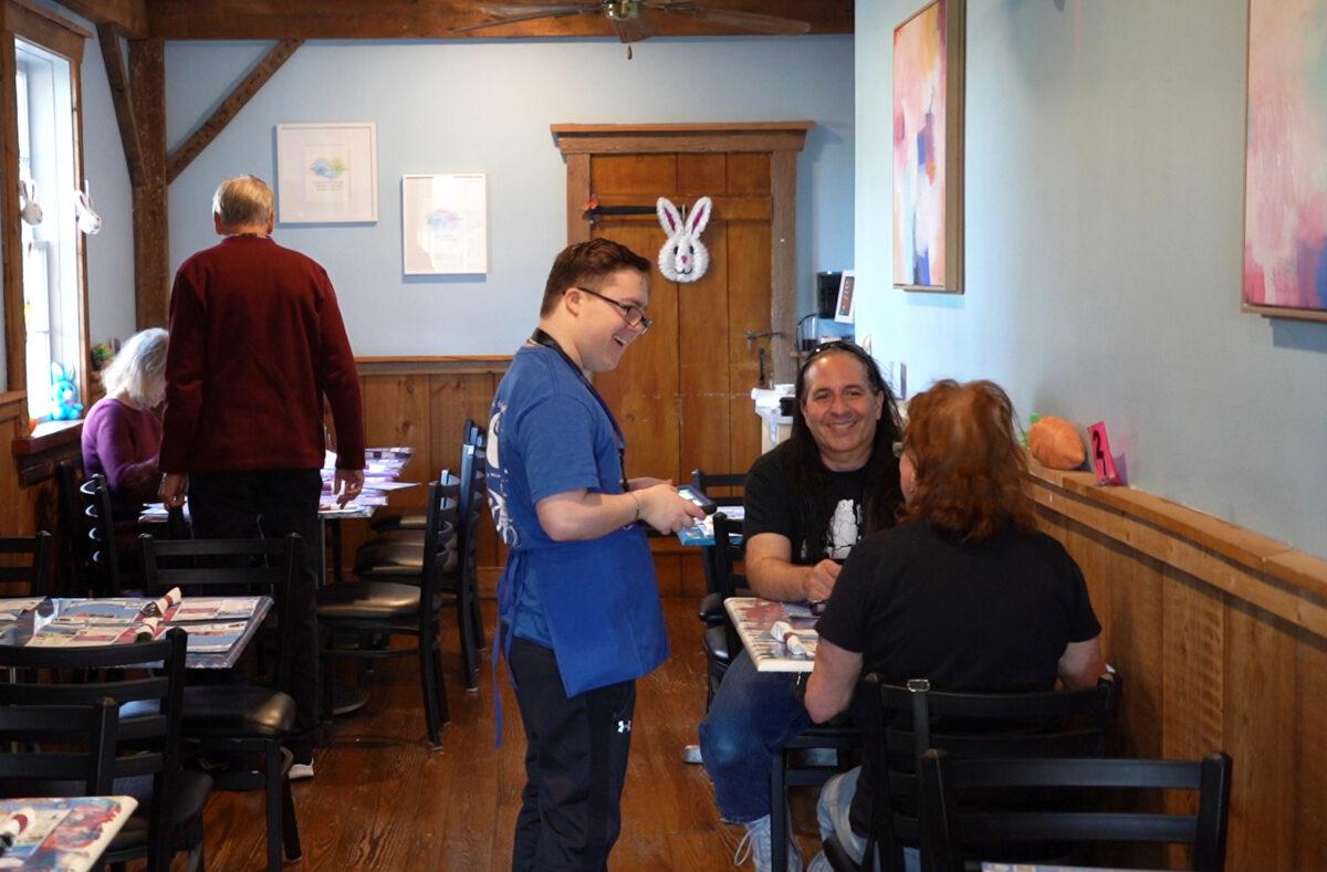 Braxton Denner, a 16-year-old server, interacts with customers at the So Much to Give Inclusive Café on March 26, 2023. (William Huang/The Epoch Times)