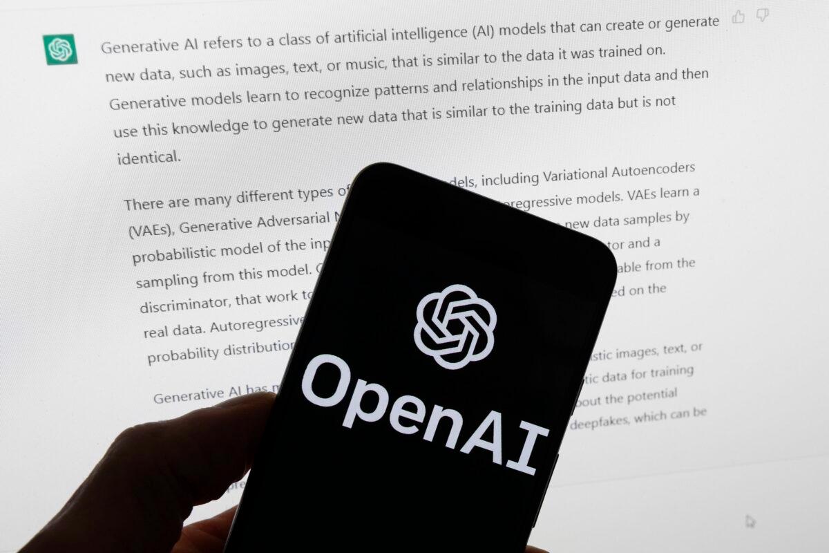 The OpenAI logo on a mobile phone in front of a computer screen displays output from ChatGPT in Boston on March 21, 2023. (Michael Dwyer/AP Photo)