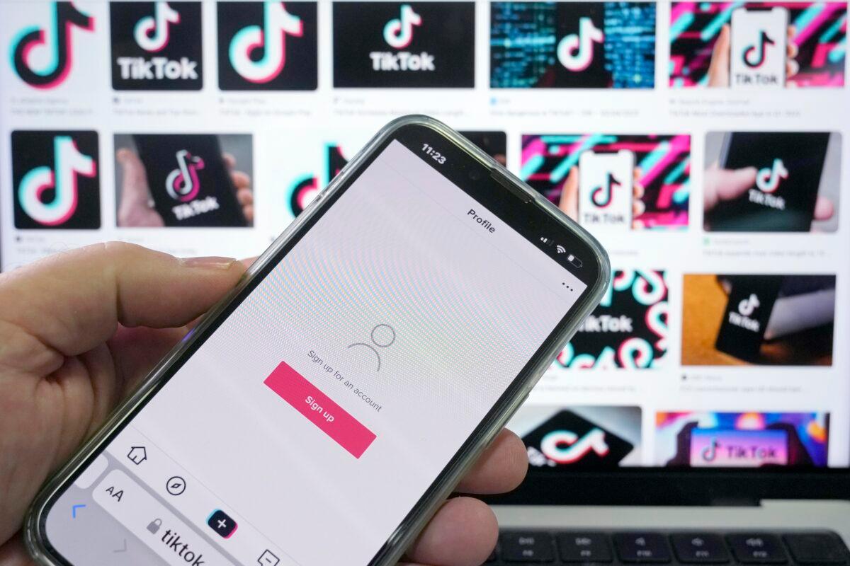 A page for the application TikTok is shown on a cell phone in front of a screen with logos for the company on April 4, 2023. (Rick Rycroft/AP Photo)