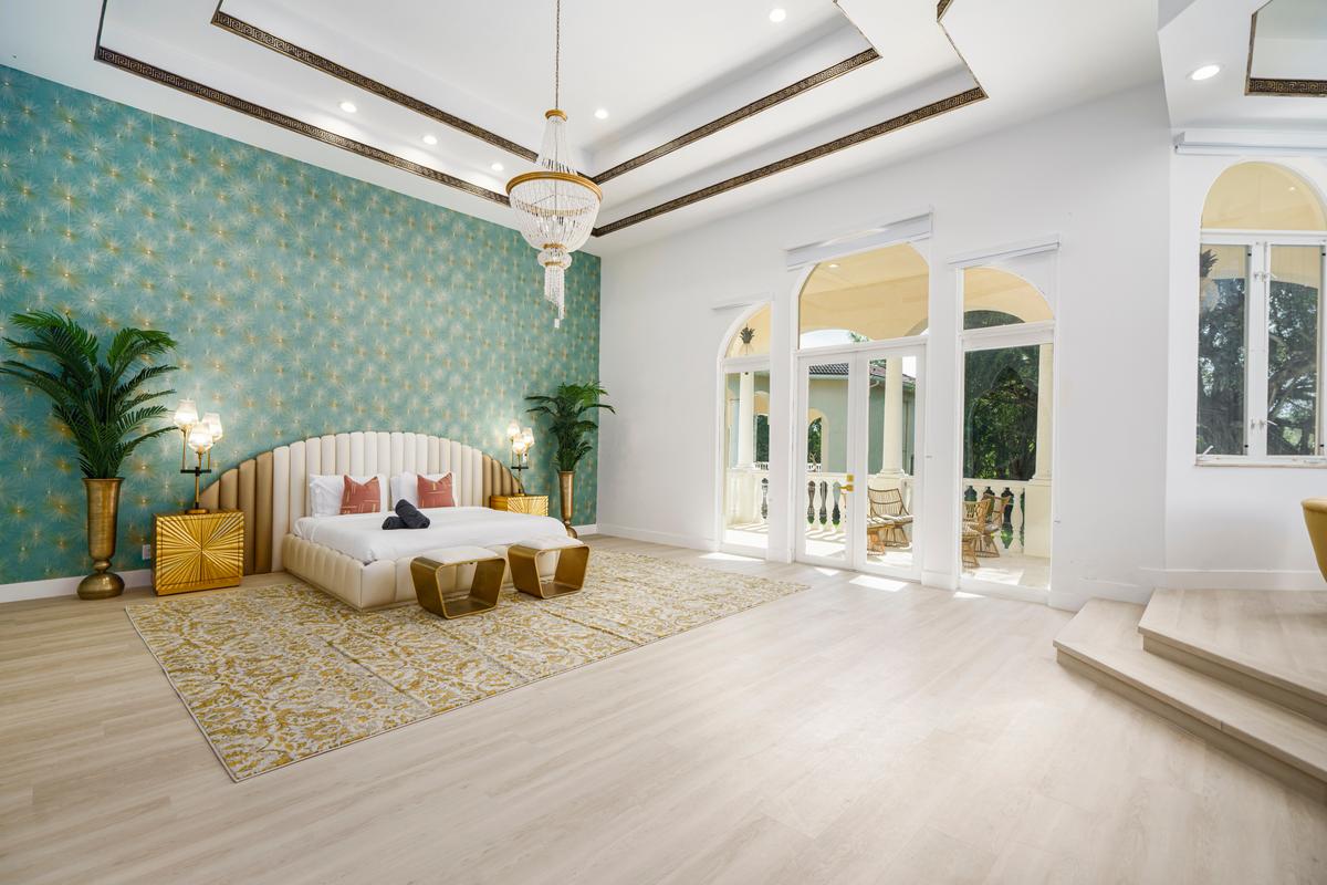 The home's master bedroom is exceptionally airy, with multi-level ceiling accents, warm wood flooring, glamorous lighting, and direct access to the pool area. (Courtesy of The Carroll Group)
