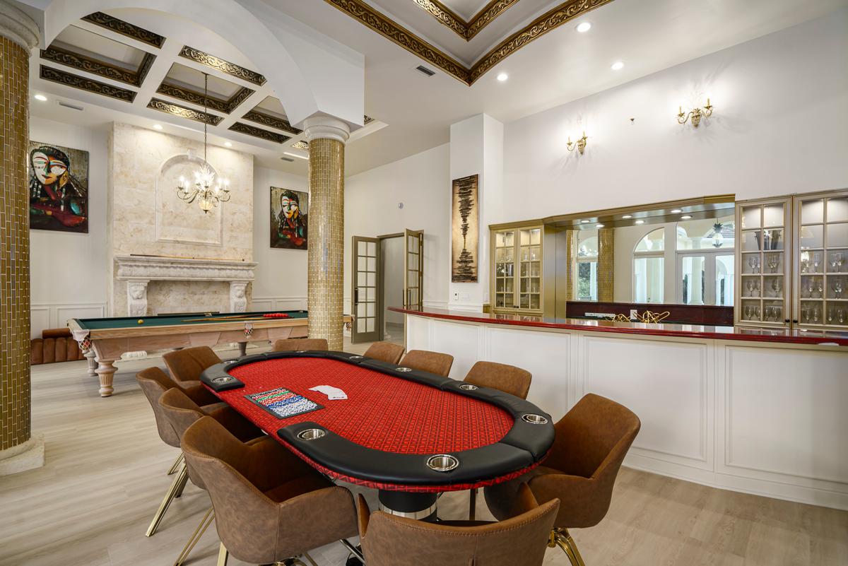 The game room features soaring ceilings, wood flooring, a wet bar, fireplace, large game table, and a billiards table. (Courtesy of The Carroll Group)