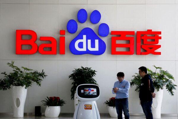 Men interact with a Baidu AI robot near the company logo at its headquarters in Beijing on April 23, 2021. (Florence Lo/Reuters)