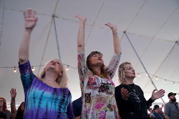 Three women hold their arms aloft in prayer during a service in Bakersfield, Calif., on March 12, 2023. (Allan Stein/The Epoch Times)