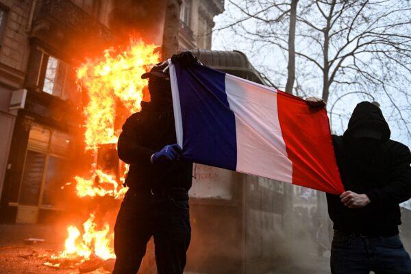 Masked protesters hold a French flag next to a burning news kiosk beside the Place de l'Opera on the sidelines of a demonstration as part of a national day of strikes and protests in Paris on March 23, 2023. (Alain Jocard/AFP via Getty Images)