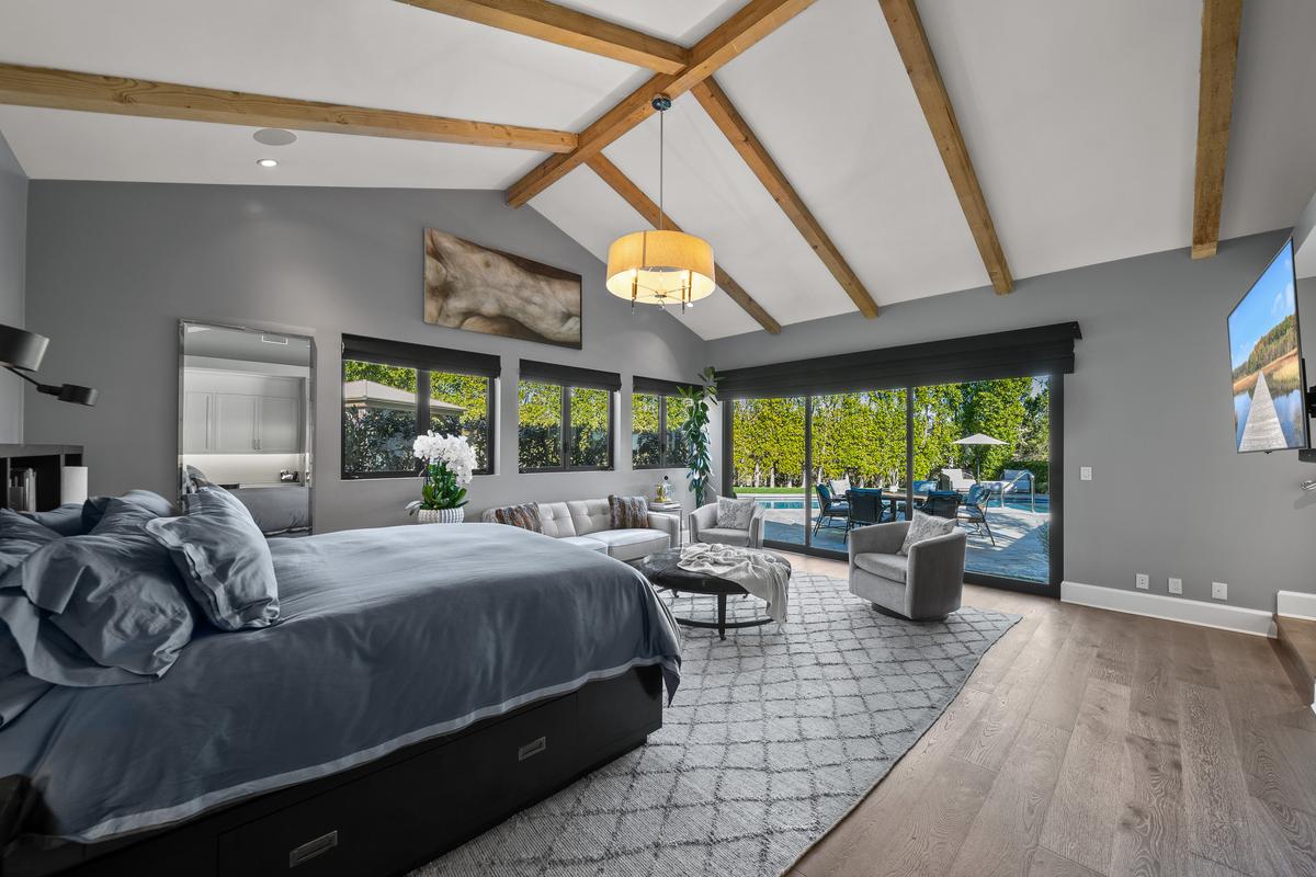 The spacious, airy master bedroom features wood flooring, a vaulted ceiling with exposed beams, and easy access to the pool and backyard amenities. (Courtesy of One Shot Productions, TopTenRealEstateDeals.com)