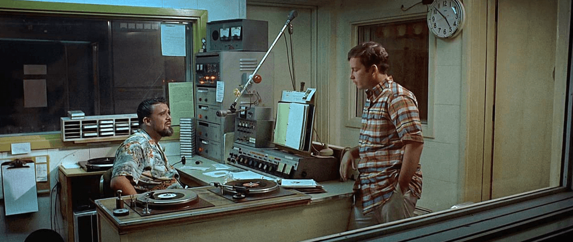 Curt (Richard Dreyfuss, R) discovers a nameless, popsicle-eating individual in a radio studio on the edge of town who gives sage advice and sounds a lot like disc jockey Wolfman Jack but claims not to be (played by Wolfman Jack himself), in “American Graffiti.” (Lucasfilm Ltd./The Coppola Company/Universal Pictures)