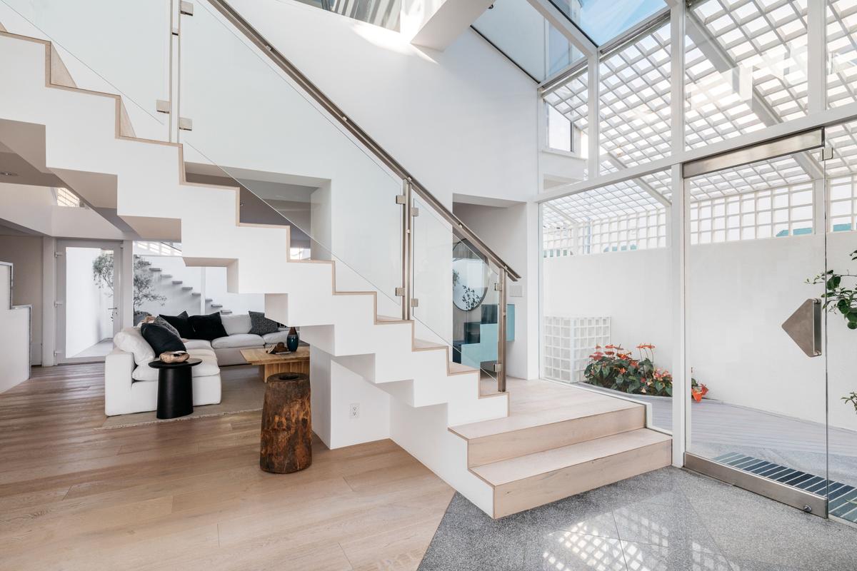 Upon stepping inside, the owners and guests are greeted by wood flooring, soaring ceilings with huge skylights, a staircase leading to the upper level, and floor-to-ceiling windows looking out over the ocean. (Courtesy of Stirling Reed and toptenrealestatedals.com)