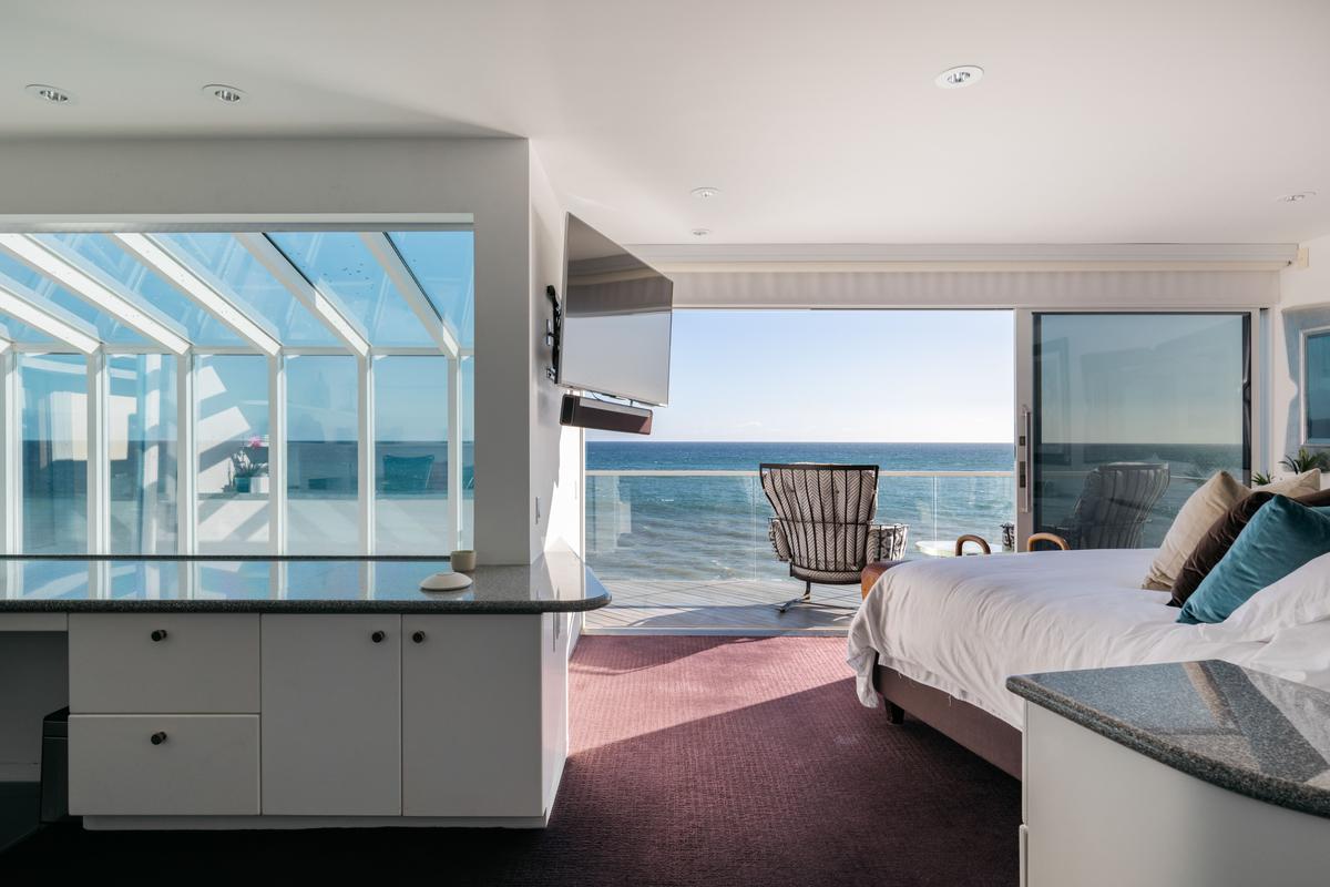 The master bedroom’s glass walls open fully for easy access to the deck overlooking the beach and ocean, with a built-in desk off to the side enjoying a most impressive view. (Courtesy of Stirling Reed and toptenrealestatedals.com)
