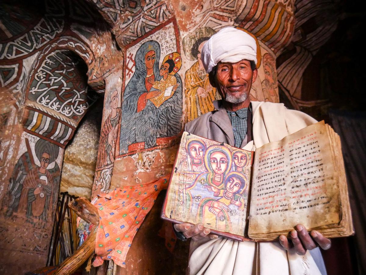 Head monastic of Abuna Yemata Guh, Priest Gebre Rufael Asresseha holds up a goatskin Bible, which has brought visitors to the church for centuries. (Kanokwann/Shutterstock)