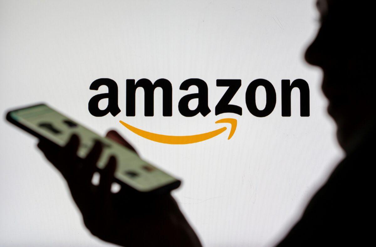 A woman with a smartphone in front of displayed Amazon logo in an illustration on July 30, 2021. (Dado Ruvic/Reuters)