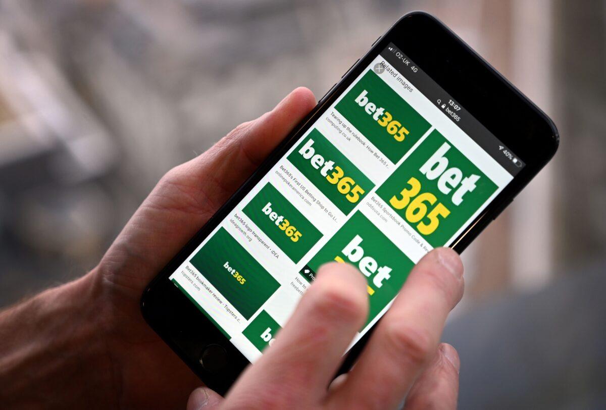 A man poses for a photograph with the logo for online gambling website Bet365 displayed on a smartphone, in London on Dec. 18, 2019. (Paul Ellis/AFP via Getty Images)