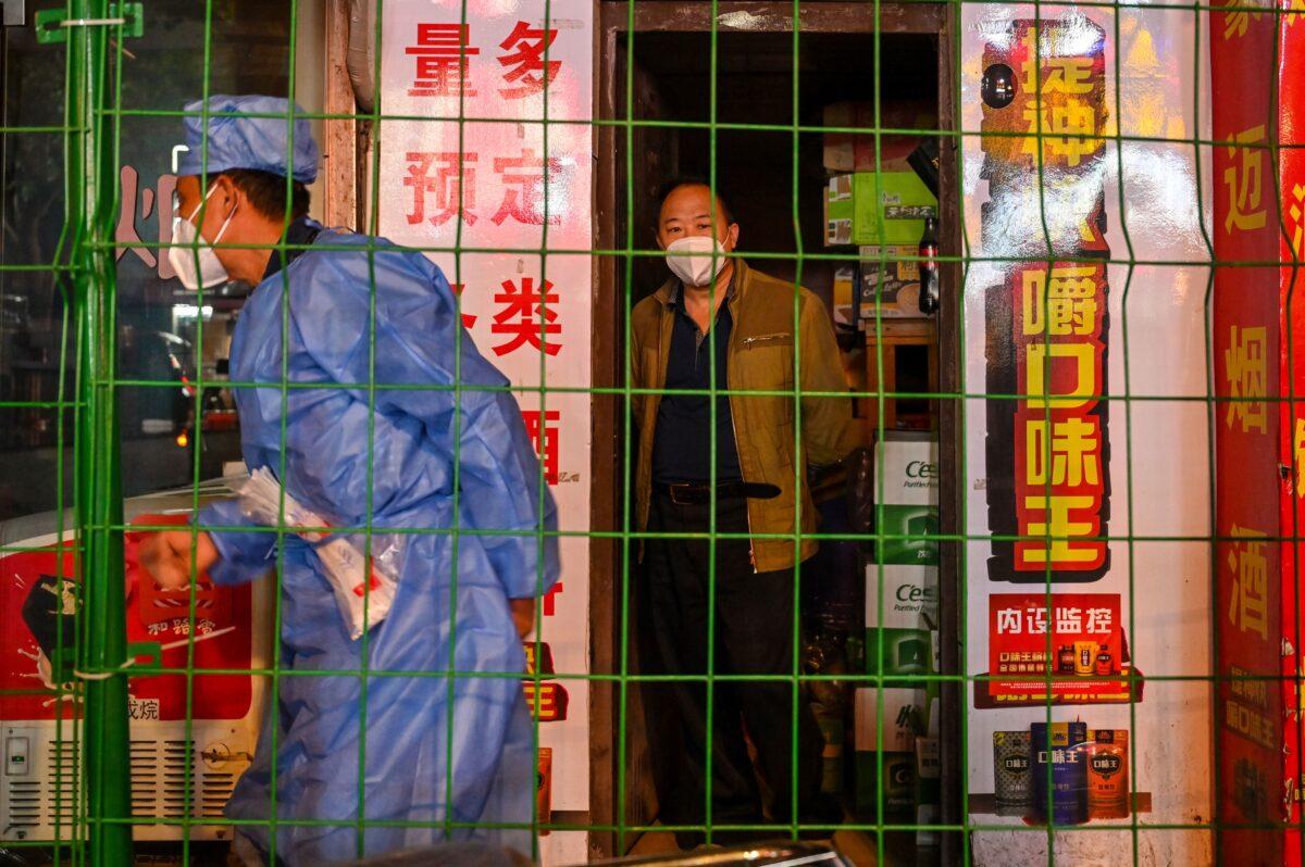 A man looks on from a shop in a locked-down neighborhood as a worker erects fencing in Shanghai's Changning district, on October 7, 2022. (Hector Retamal/AFP via Getty Images)