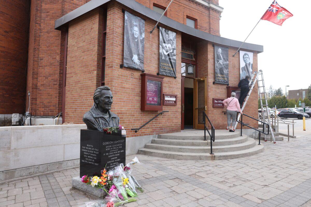 Flowers sit by a bust of Gordon Lightfoot outside the Orillia Opera House as staff change signage to honour the singer-songwriter in his hometown of Orillia, Ont., on May 2, 2023. The legendary Canadian musician passed away at 84 years old May 1, 2023. (The Canadian Press/Christopher Drost)