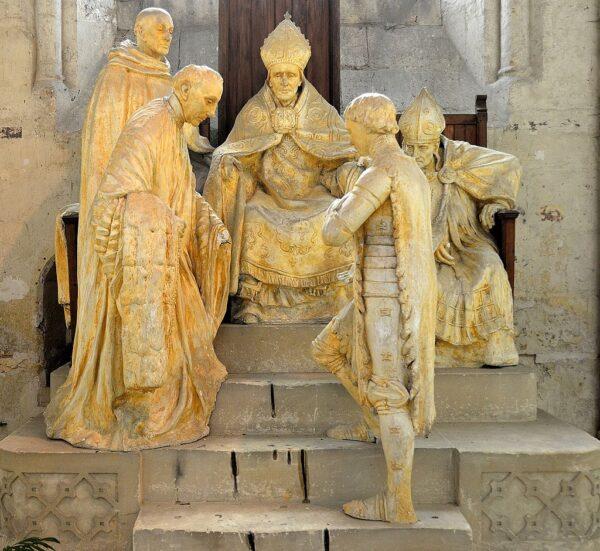 Joan in the foreground, facing figures from her trial in the monument commemorating Joan of Arc, 1909, a plaster work by Émile Pinchon. in the Cathedral of Notre-Dame at Noyon. (Public Domain)