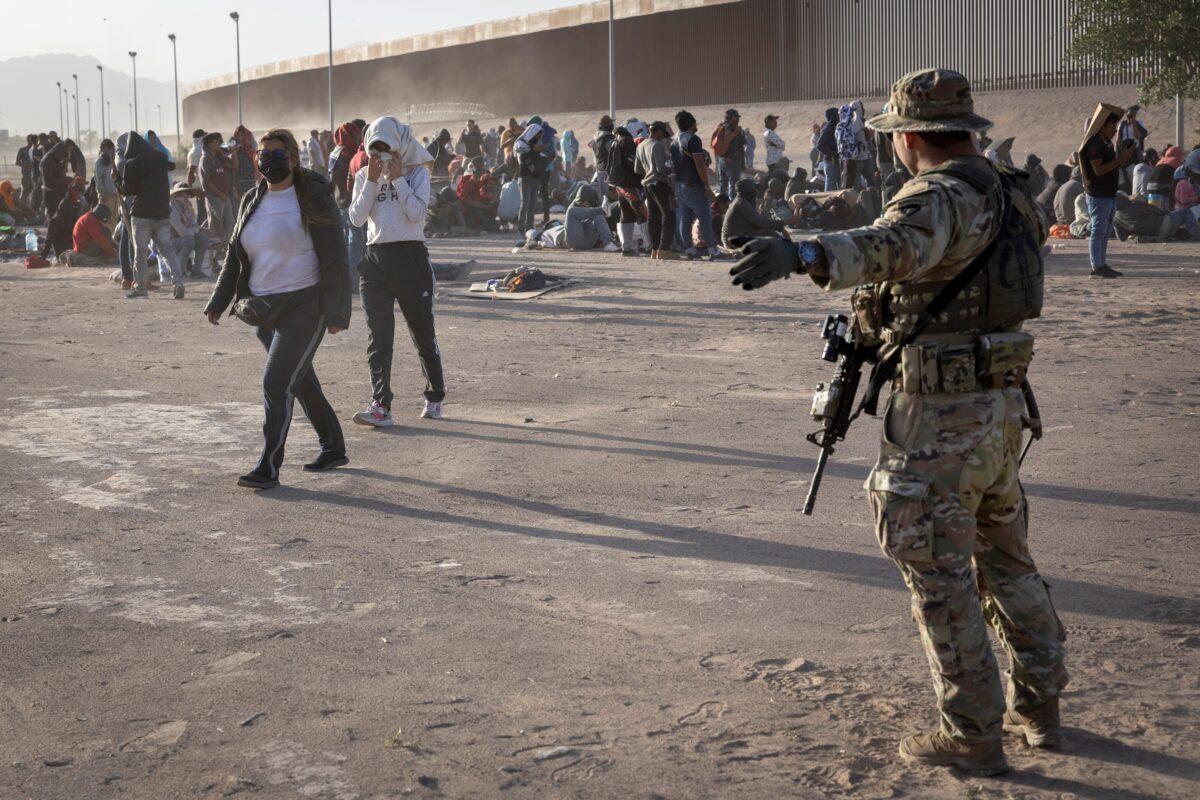 A Texas National Guard soldier directs migrants during a dust storm at a makeshift camp located between the Rio Grande and the U.S.–Mexico border fence in El Paso, Texas on May 10, 2023. (John Moore/Getty Images)