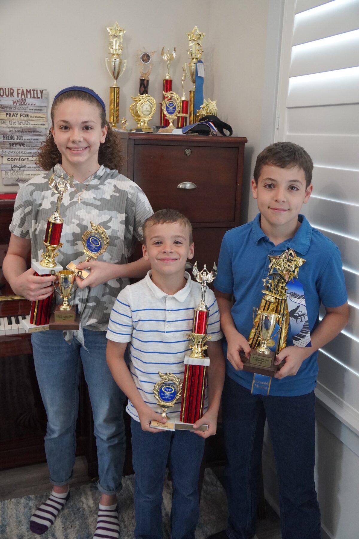 Grace Diaz (L) and brothers Royce (C) and Roark hold some of their state music competition trophies at their home in Gainesville, Fla., on April 10, 2023. (Nanette Holt/The Epoch Times)