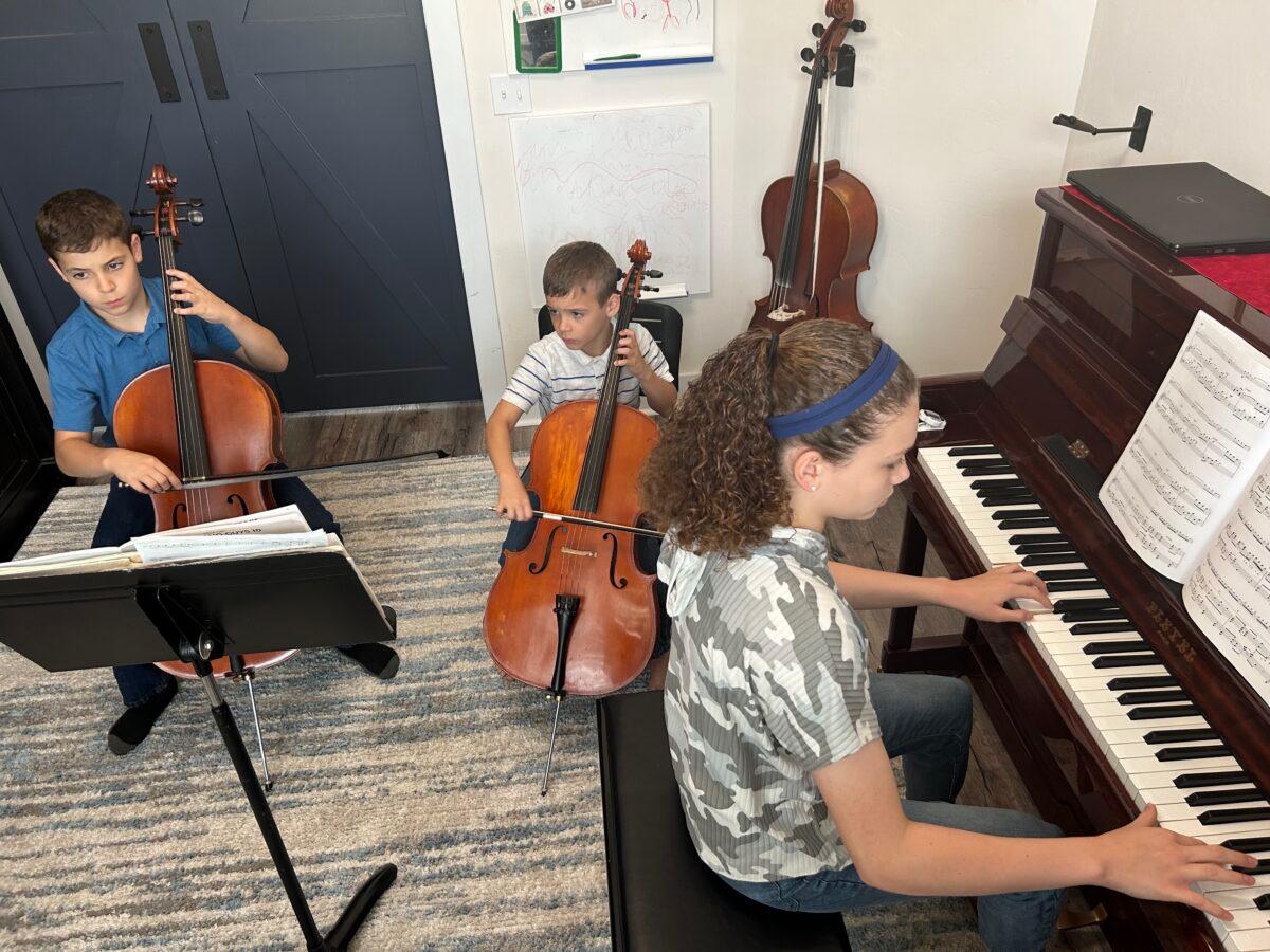 Roark Diaz (L) and his brother, Royce, accompany their sister, Grace, in playing a Piano Guys composition called "A Sky Full of Stars" at their home in Gainesville, Fla., on April 10, 2023. (Nanette Holt/The Epoch Times)