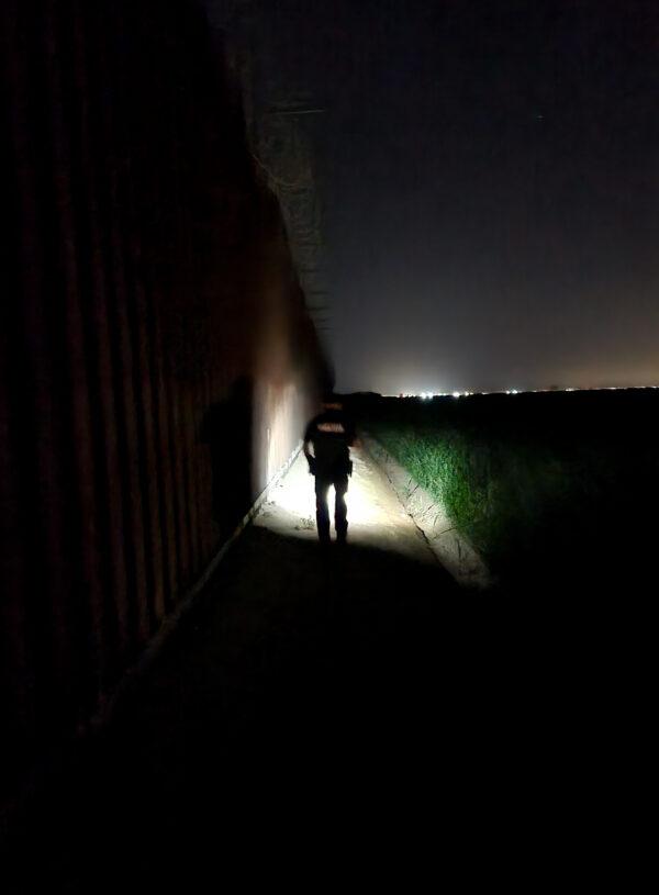 San Luis, Ariz., Police Lt. Marco Santana walks along a dirt section to speak with illegal immigrants on the Mexico side of Arizona's southern border fence on May 11, 2023. (Allan Stein/The Epoch Times)