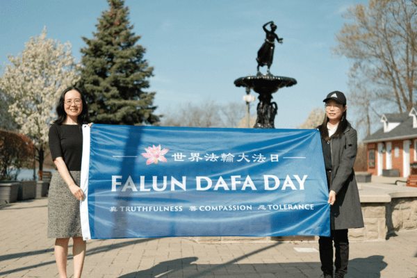 Falun Gong practitioners Carolyn Jin (L) and Melissa Li hold a Falun Dafa flag in Amherstburg, Ontario on May 5, 2023, to celebrate the 31st anniversary of World Falun Dafa Day. (The Epoch Times)