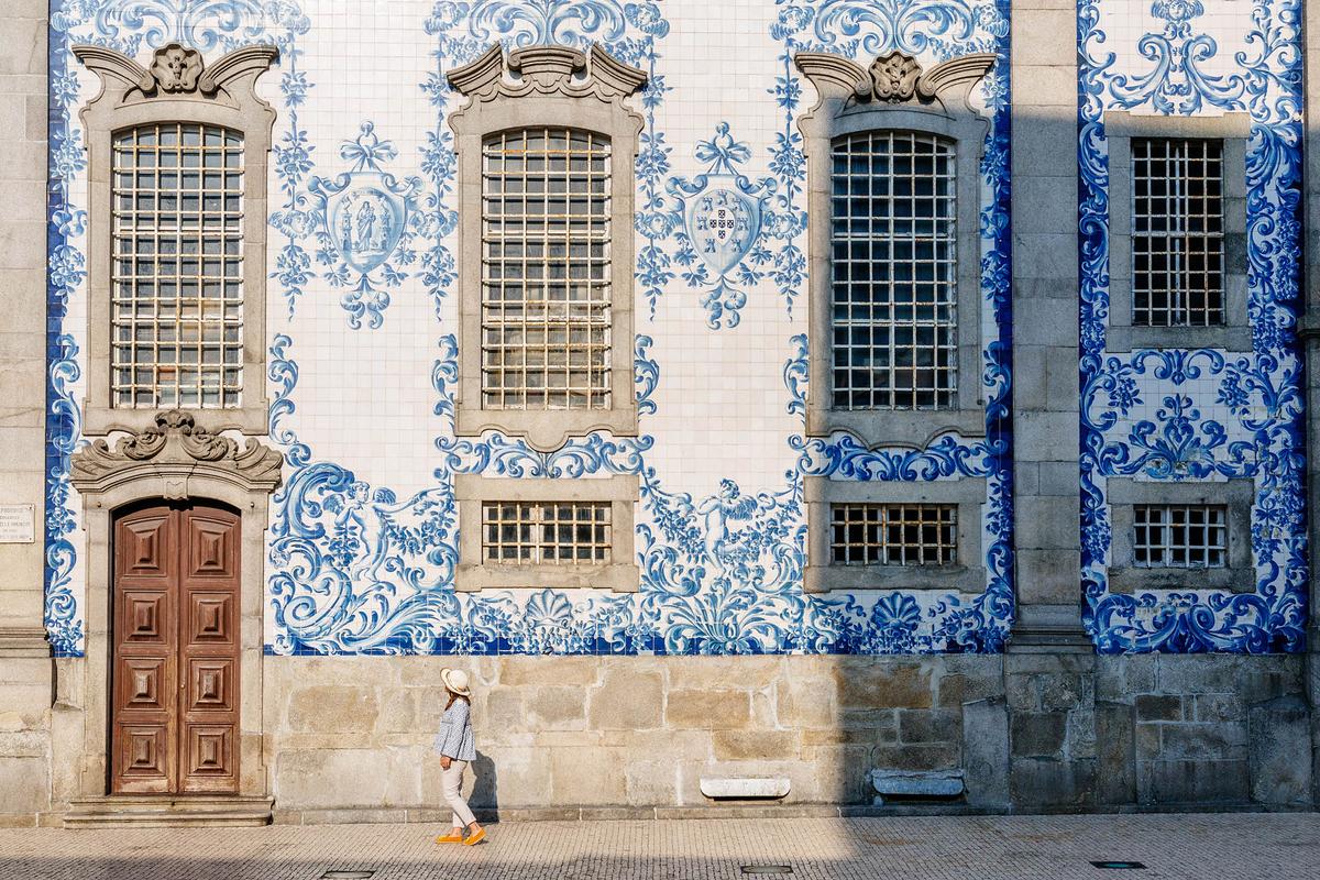 A woman examines the azulejos tile artwork on the side of Chapel Of Souls in Porto, Portugal (iacomino FRiMAGES/Shutterstock)