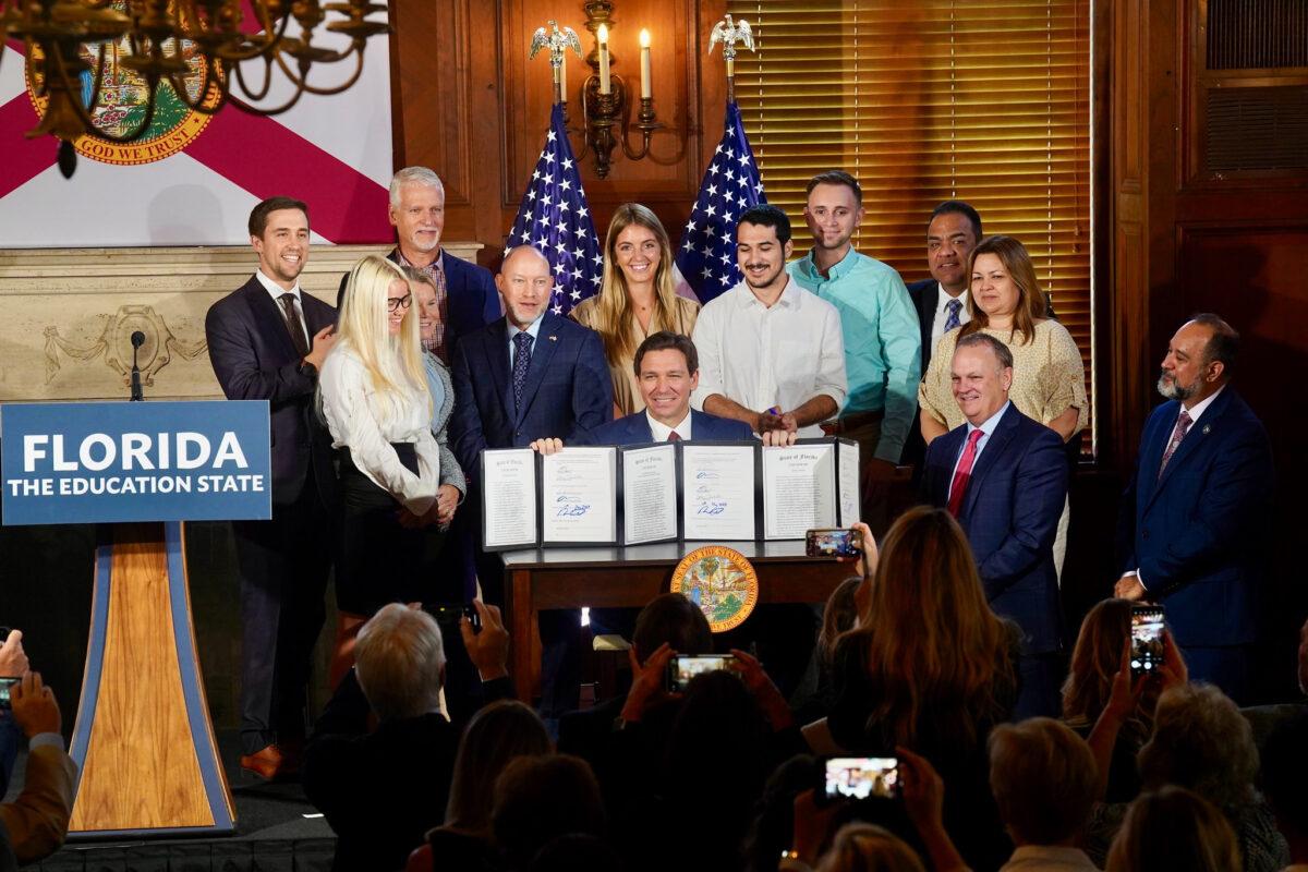 Florida Gov. Ron DeSantis holds up three just-signed bills related to higher education in the state—including one that bans diversity, equity, and inclusion practices—at New College in Sarasota, Fla., on May 15, 2023. (Courtesy of the Florida Governor's Office)