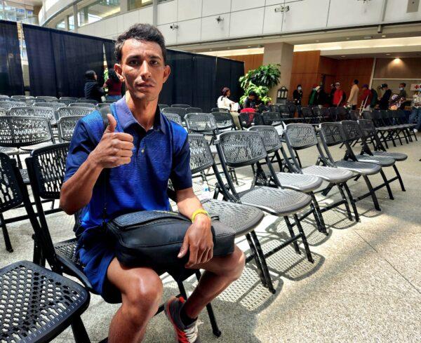 Alexander, a Venezuelan national, gives a cautious thumbs-up while waiting for a bus at the Denver Reception Center on May 17, 2023. (Allan Stein/The Epoch Times)