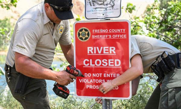 Fresno County Sheriff's Office reservists attach a sign to a post to alert people that the Kings River is closed due to dangerously high water levels near Sanger, Calif., on May 22, 2023. (Craig Kohlruss/The Fresno Bee via AP)