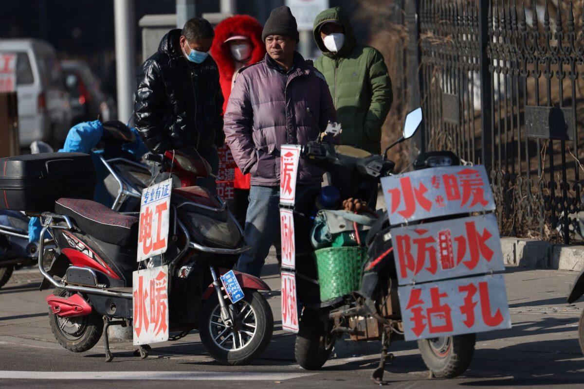 Migrant workers standing near signs advertising their skills as they wait by a street to be hired in Shenyang, Liaoning Province, China, on Feb. 6, 2023. (STR/AFP via Getty Images)