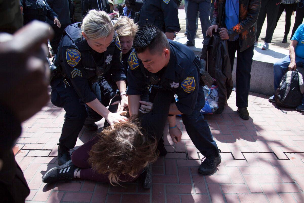 A woman who allegedly threw a brick toward the front of the crowd is tackled by San Francisco police officers, in San Francisco on May 23, 2023. (Lear Zhou/The Epoch Times)
