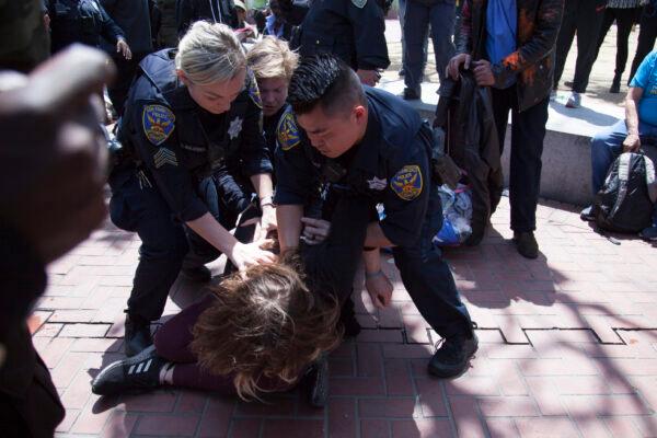 A woman who allegedly threw a brick toward the front of the crowd is tackled by San Francisco police officers. (Lear Zhou/The Epoch Times)